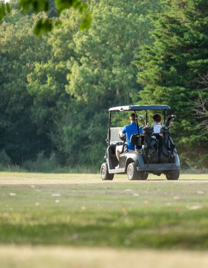 Two men in a dark green golf buggy, driving across the golf course.