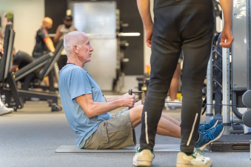An elderly gentlemen, having a personal training session, using the cable machines.
