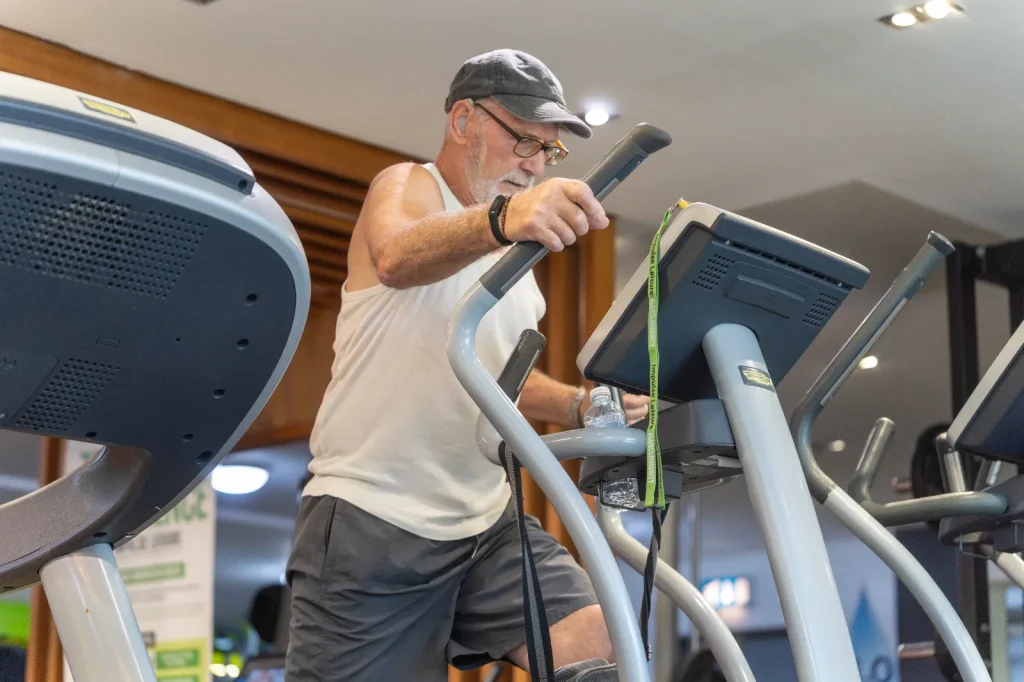 Older man using a Technogym cross trainer during a cardio workout at the gym
