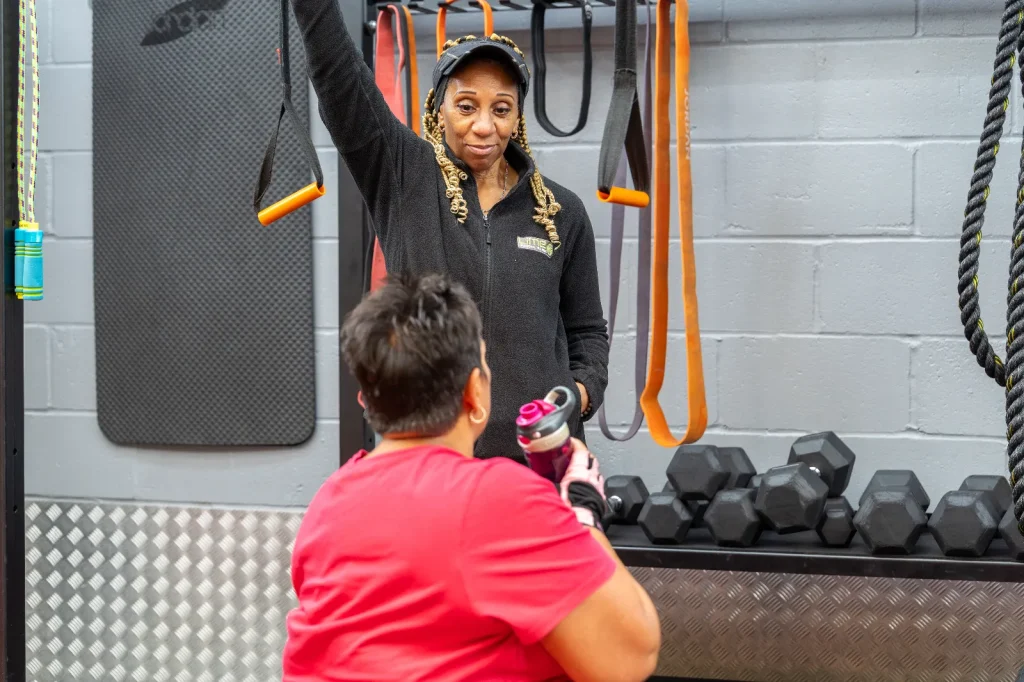 Lime personal trainer demonstrating an exercise to a client in the functional training area at Blackshots gym