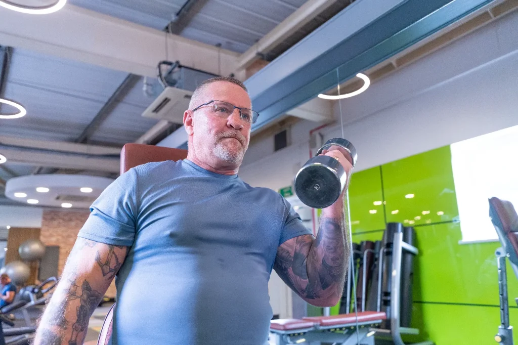 Man performing a dumbbell curl exercise in the free weights area of a leisure centre gym