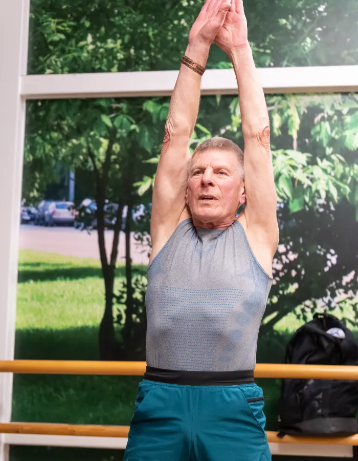 Older man stretching overhead during a group fitness class at a leisure centre studio