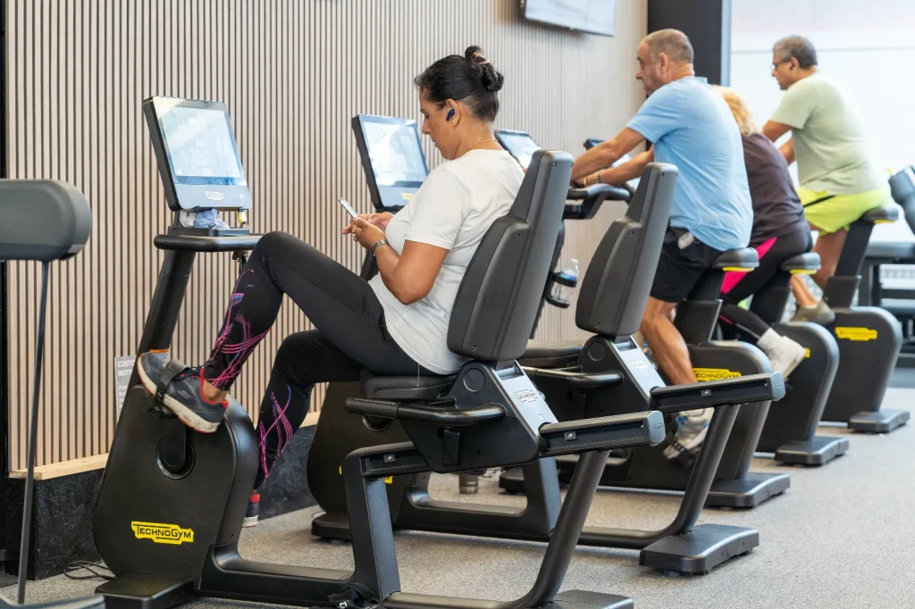 Members using Technogym recumbent exercise bikes in a busy gym cardio area