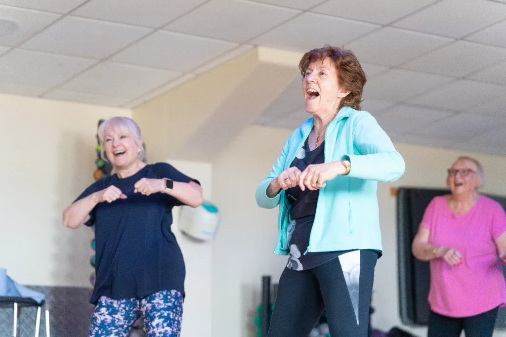 Two older women laughing and dancing during a dance fitness class at an Impulse Leisure centre