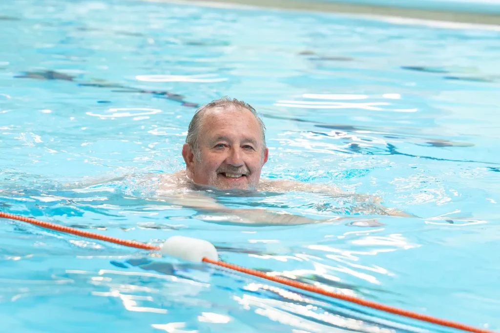 Older man smiling while swimming a lane during adult swimming lessons at an Impulse Leisure centre