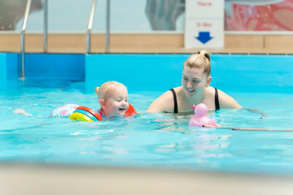 Parent and toddler enjoying a baby and toddler swimming lesson at an Impulse Leisure pool, with the child wearing colourful armbands