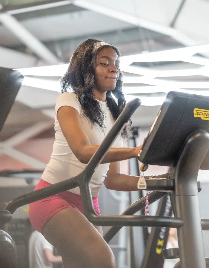 Young woman smiling while using a cardio machine at Blackshots Impulse Leisure gym, with another member exercising in the background