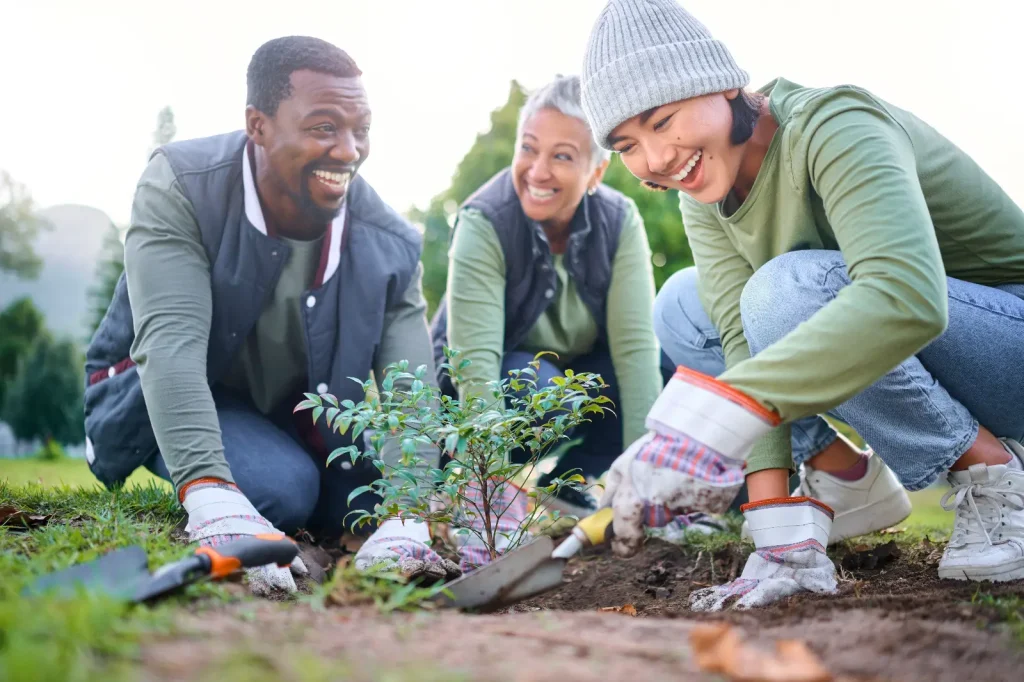 Three smiling volunteers planting a small tree together in a community garden