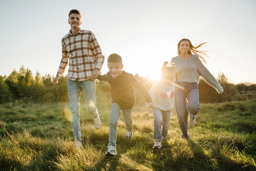 a family, holding hands, running across a field on a sunny day.
