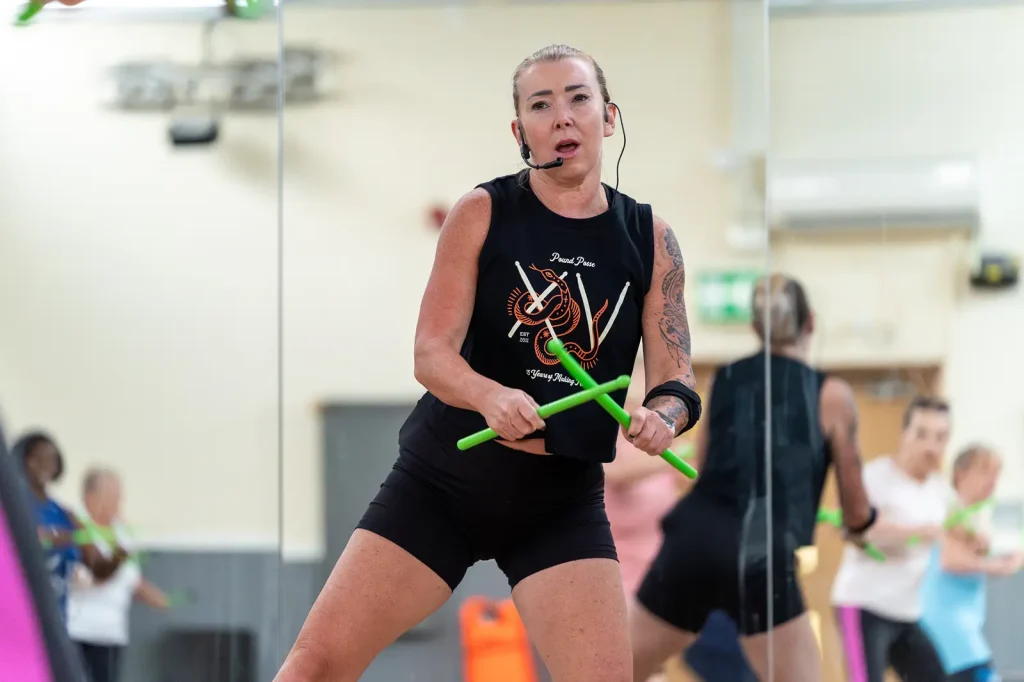 A female dance fit instructor, stood at the front of the class giving a demonstration.