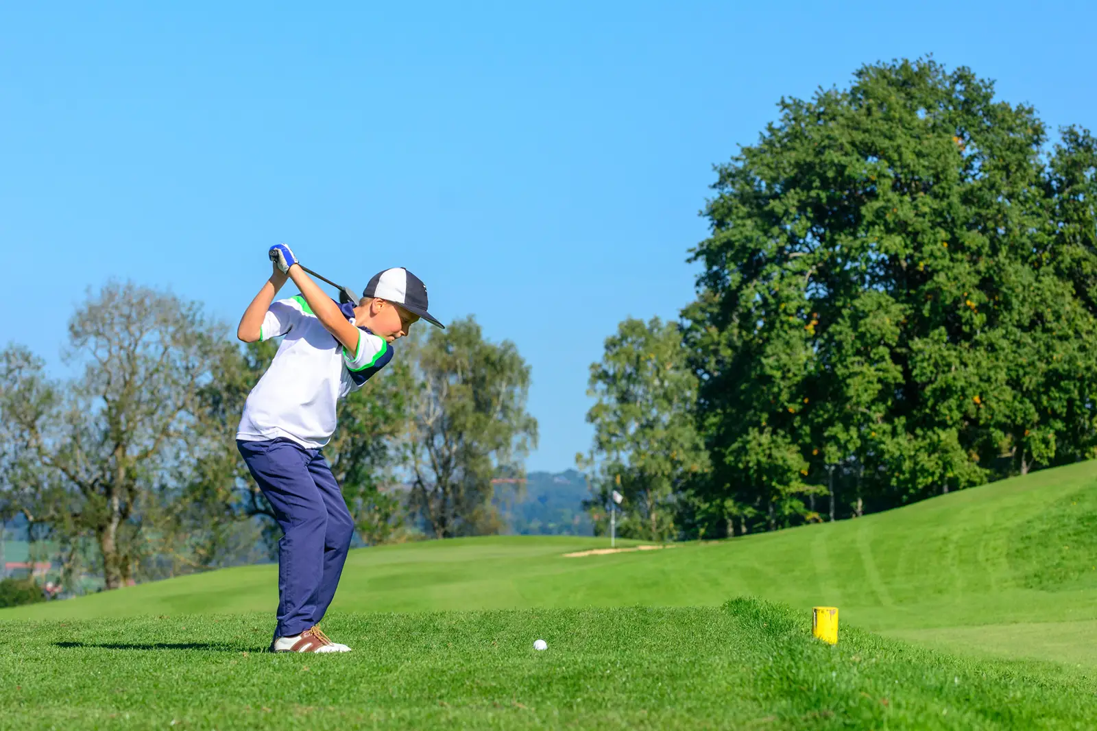 A young boy, preparing to swing the golf club towards the golf ball