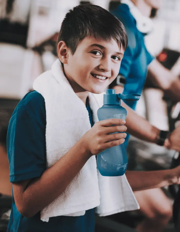 Smiling boy holding water bottle with towel around neck during junior gym session at Corringham