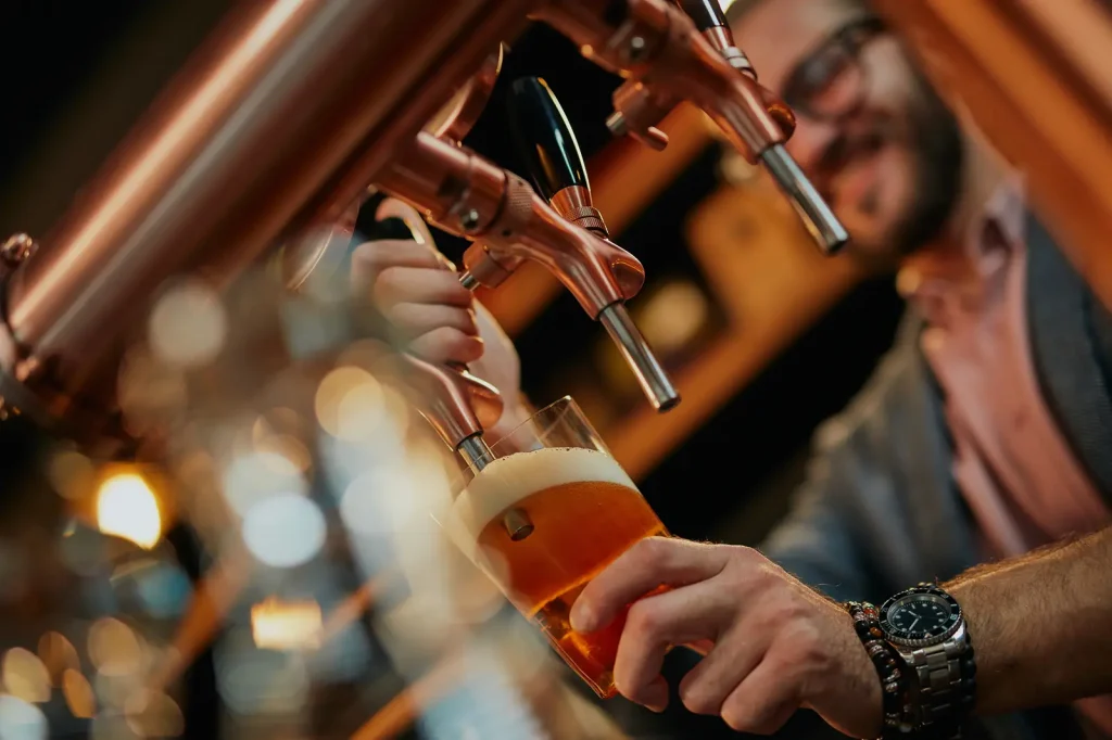 Bartender pouring a pint of craft beer from copper draft taps