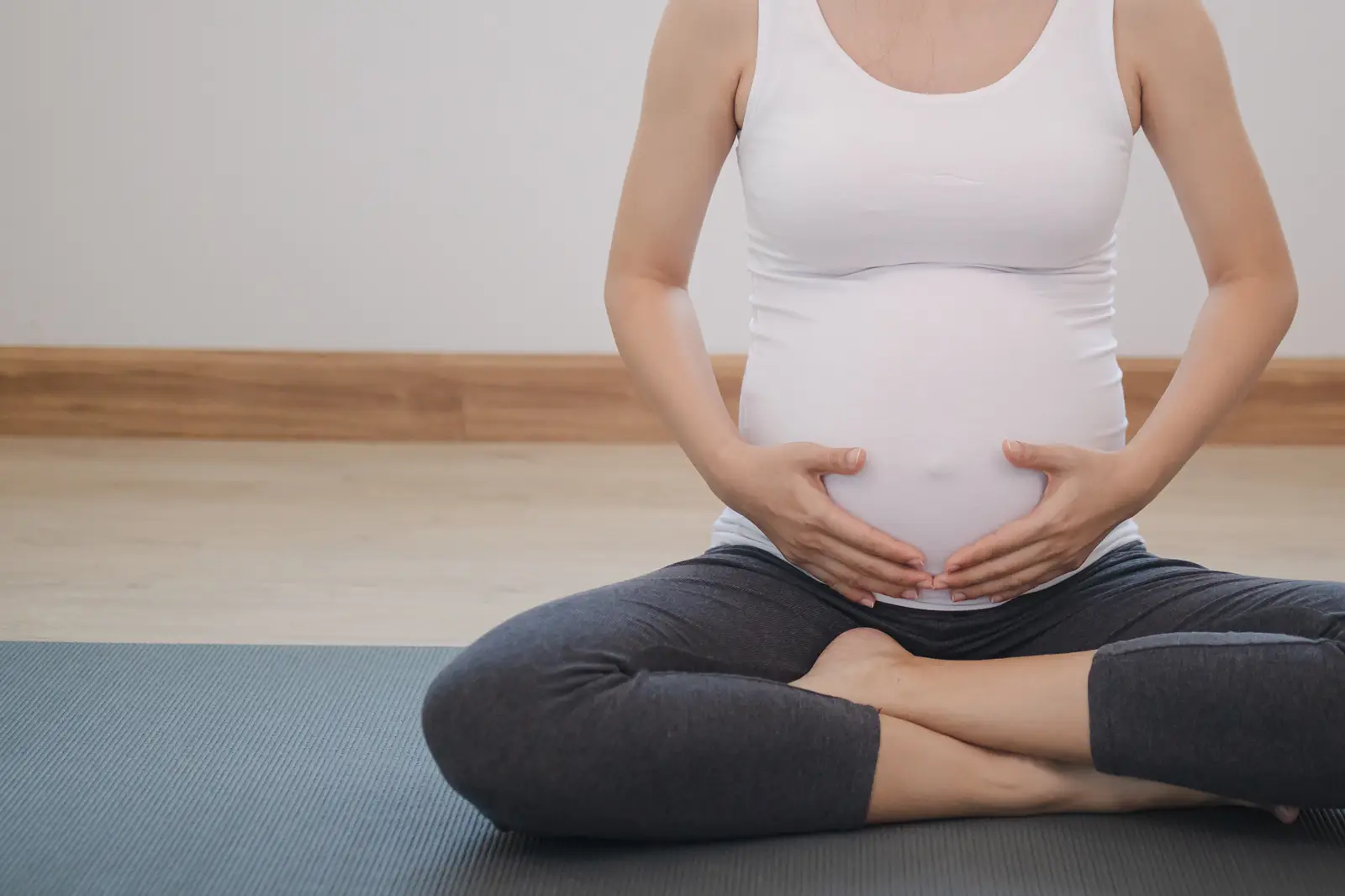 pregnant lady sat cross legged on a yoga mat, holding her bump.